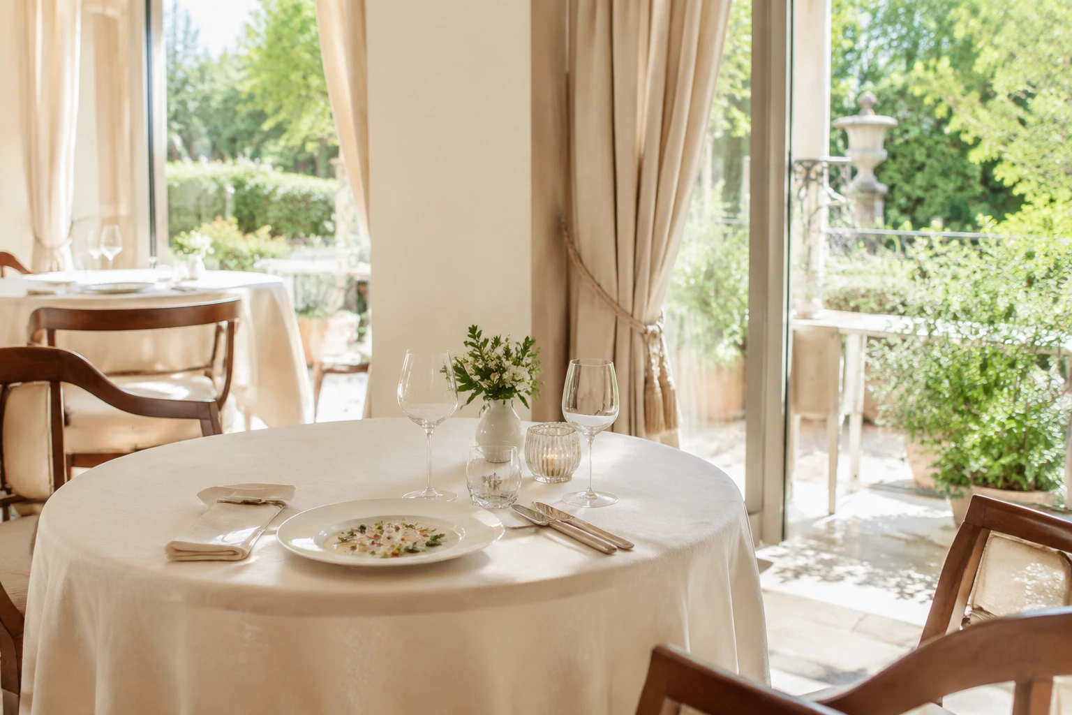 Bàn ăn fine dining tinh tế trong nhà hàng sáng với cửa nhìn ra vườn